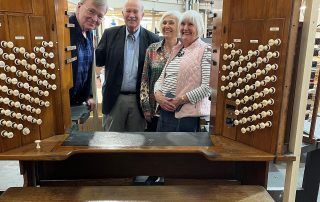 Four people look through the console of an organ, with a set of organ stops visible on each side of them