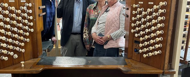 Four people look through the console of an organ, with a set of organ stops visible on each side of them