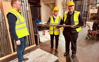 Three people wearing hi-vis jackets. Two are smiling and holding an organ pipe