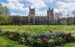 Bristol Cathedral on a bright spring day, with a green in front and a bed of spring flowers in the foreground.